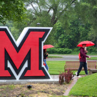 Students walking on campus near a life-size Miami Beveled M sign