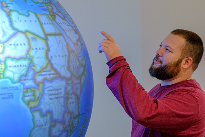 Tyler Judd pointing at a giant globe