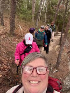 A selfie of Move Beyond Surviving (MBS) women walking in a line along an outdoor trail, With green trees in the background.
