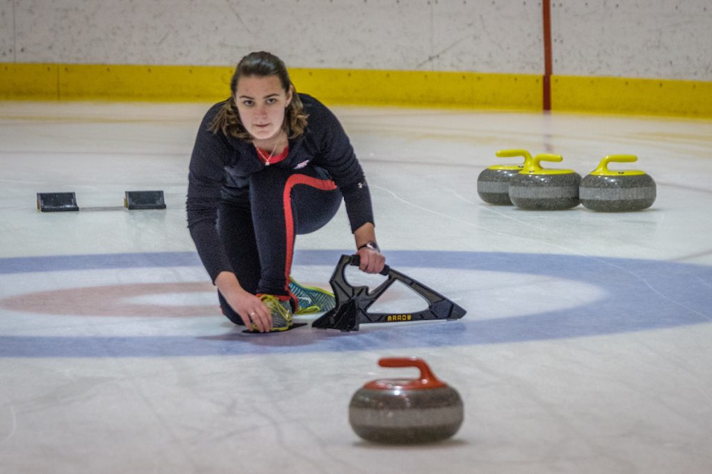 girl with all black outfit throwing a curling stone down the ice at Goggin