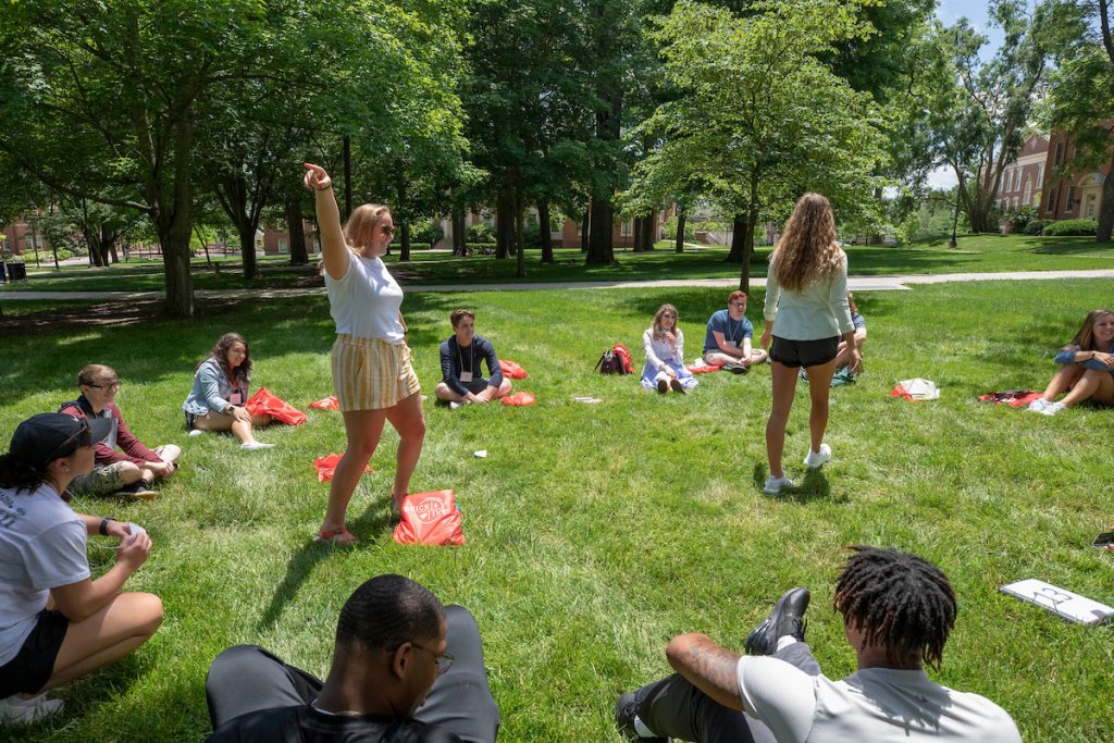 two female student orientation leaders stand in the center of a circle of other college students