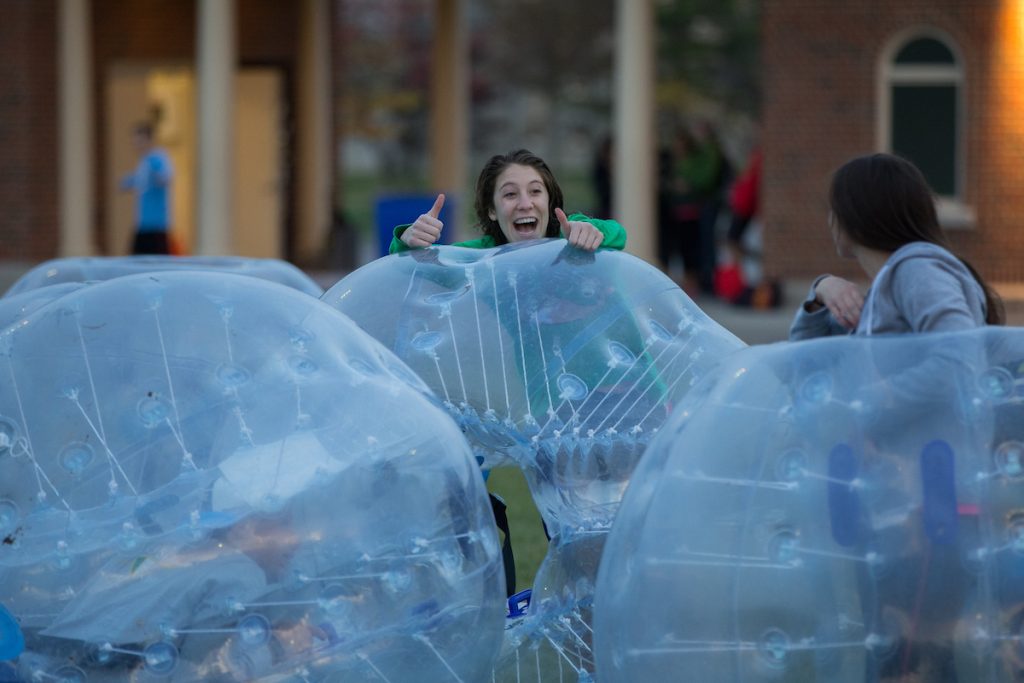 A girl sticking her head out of a giant hamster ball giving two thumbs up 