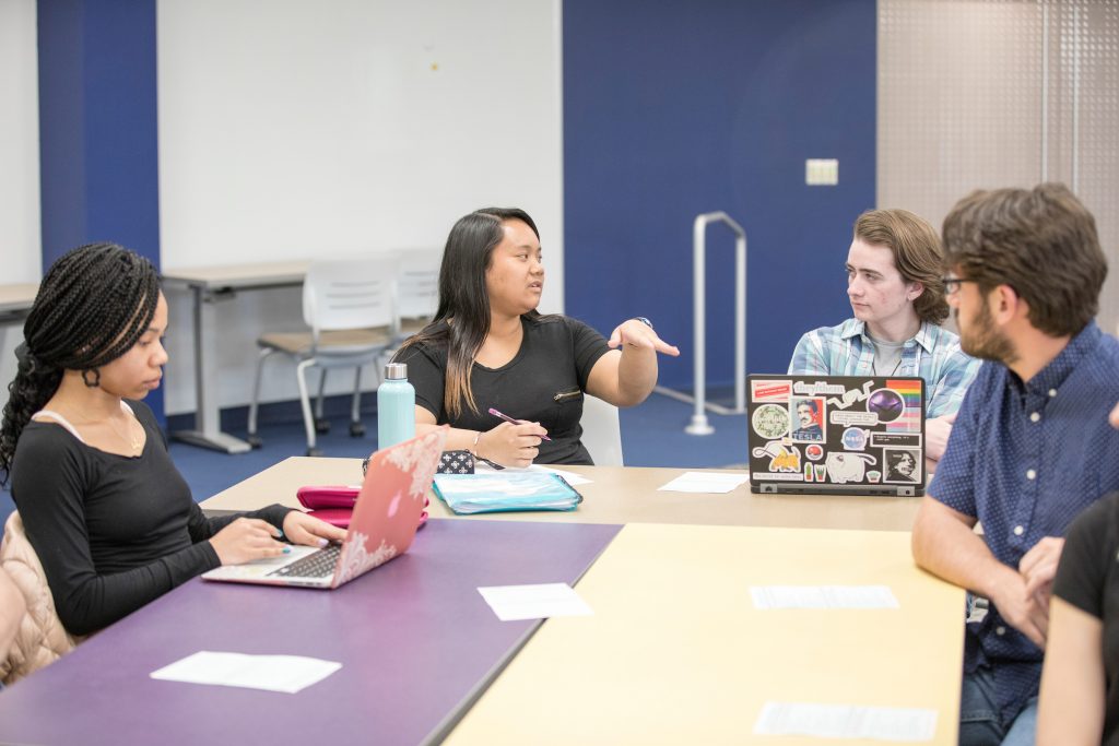 four students at a long table having a discussion at the Howe Writing Center.