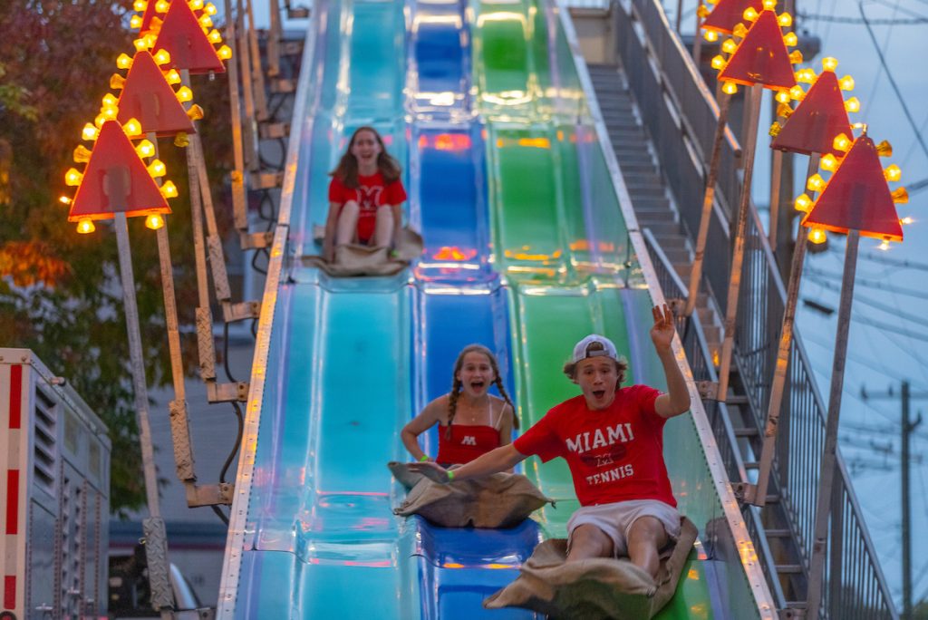 three students in Miami t-shirts going down a blue and green fun slide