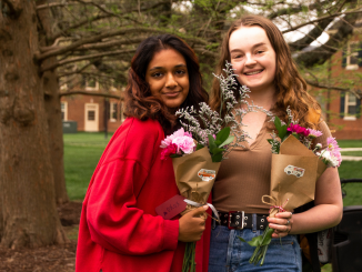two students on central quad, holding up bouquets of flowers