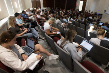 Large lecture hall filled with students who have notebooks and computers out