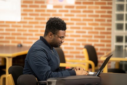 A student working on his laptop at a table.