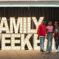 Family of four people standing in front of a LED sign that says Family Weekend